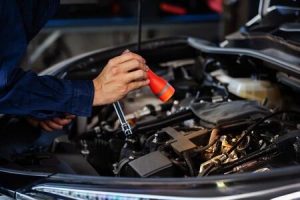 A man looks into the hood of a car with a flashlight