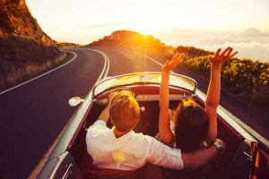 A man and woman ride in a vintage sports car on an open road