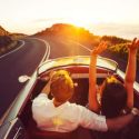 A man and woman ride in a vintage sports car on an open road