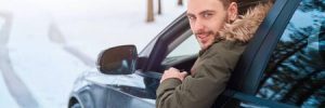 A man leans out of the driver side window of a vehicle while driving in the snow