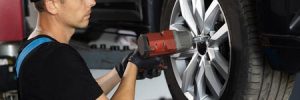 A mechanic works on a car's tire with a drill