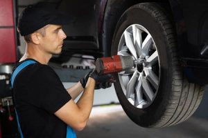 A mechanic works on a car's tire with a drill