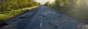 A road in poor condition with potholes and other issues