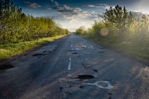 A road in poor condition with potholes and other issues