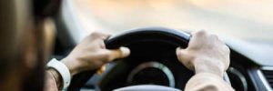 A young man holds the wheel in the correct manner while driving down an open road