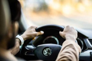 A young man holds the wheel in the correct manner while driving down an open road